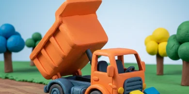 粘土細工で作られたオレンジ色のダンプトラックとカラフルな積み荷（クレイアニメ風）